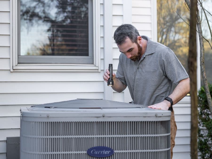 An HVAC technician servicing an outdoor air-conditioning unit — local home-service work